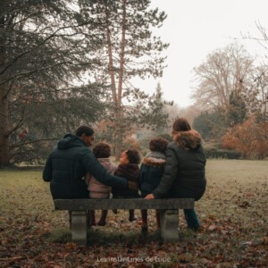 Une famille, assise sur un banc et photographiée de dos par les Instantanés de Lucie.